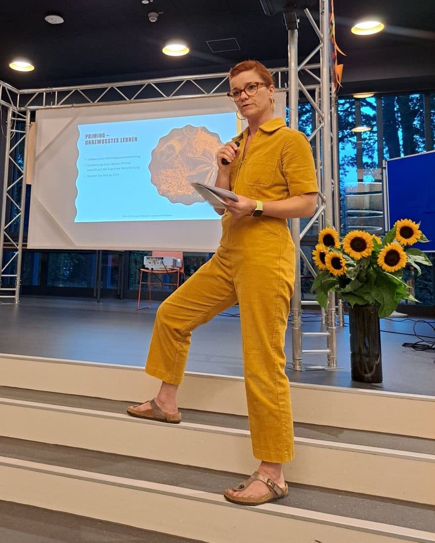 Christiane Schmieder spricht auf einer Bühne, hinter ihr eine Folie zum Thema Priming